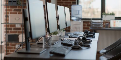 Nobody in empty call center workstation with computers and audio instruments. No people at customer service office desks with telecommunications technology, offering helpline assistance.